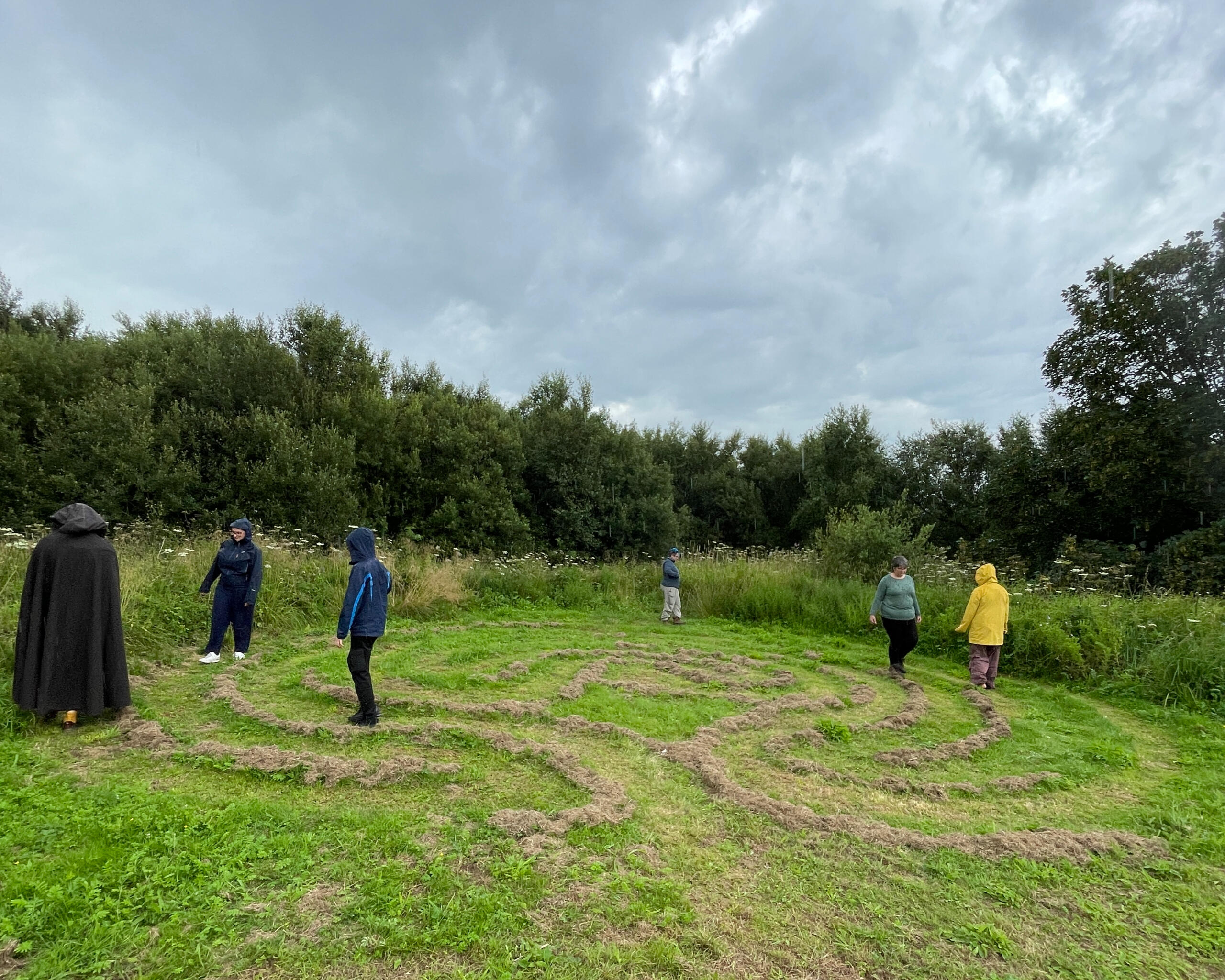 Classical pattern labyrinth mown into the lawn. Several participants are walking it in the rain.